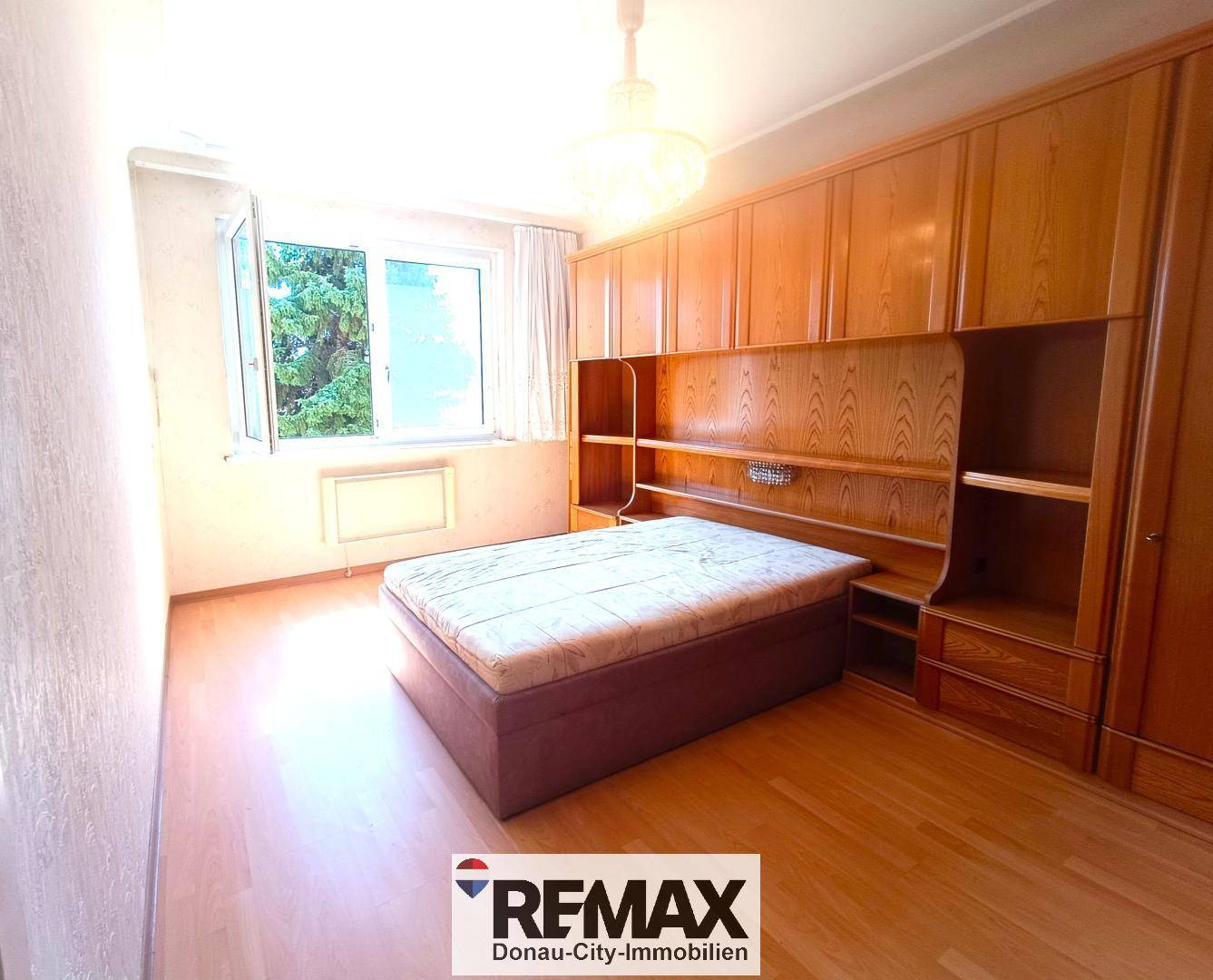 Schlafzimmer mit Holzeinbauschränken, Bett und Fenster mit Blick ins Grüne.