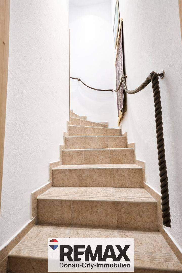 Treppenaufgang mit gefliesten Stufen und einem Seilgeländer, das nach oben führt.