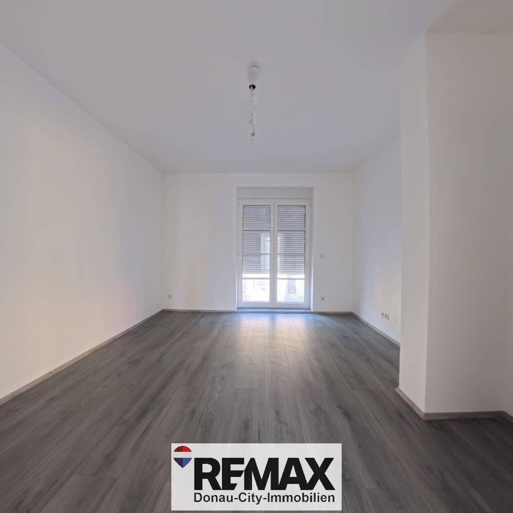 Heller Raum mit großem Fenster und grauem Laminatboden, ideal als Schlaf- oder Arbeitszimmer.