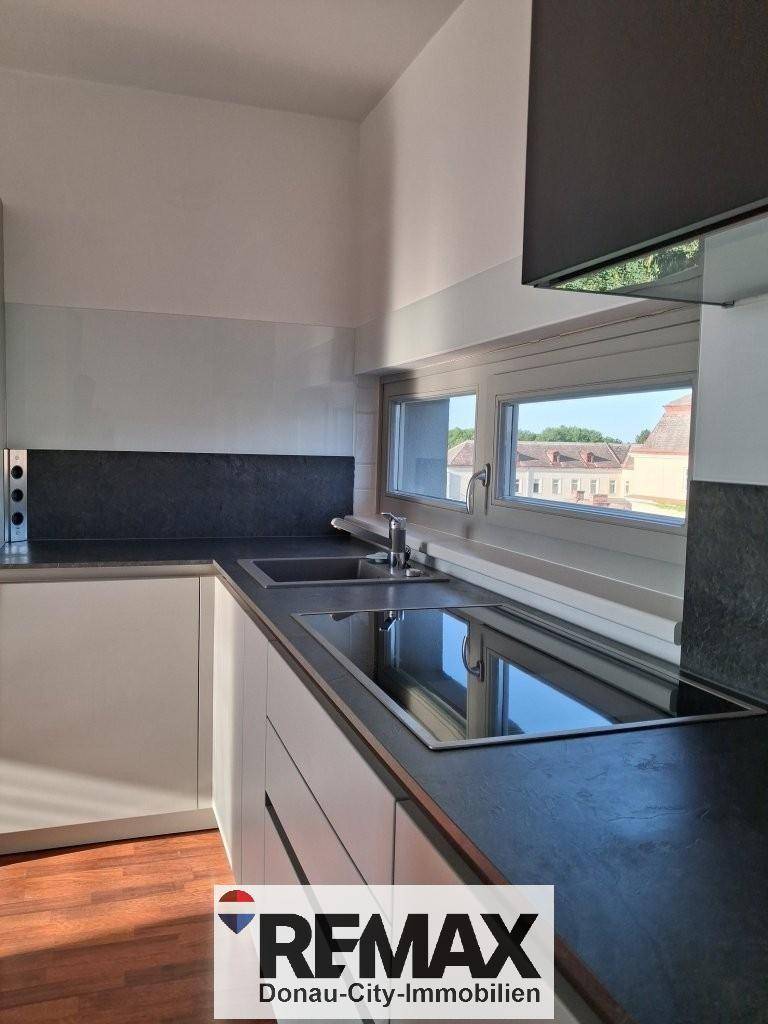 Moderne Einbauküche mit Induktionskochfeld, Spüle und Fenstern, die viel Tageslicht hereinlassen.