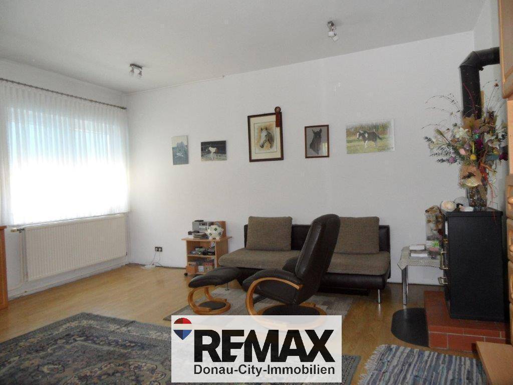 Gemütliches Wohnzimmer mit Sofa, Sessel, Holzfußboden und einem sichtbaren Holzofen.