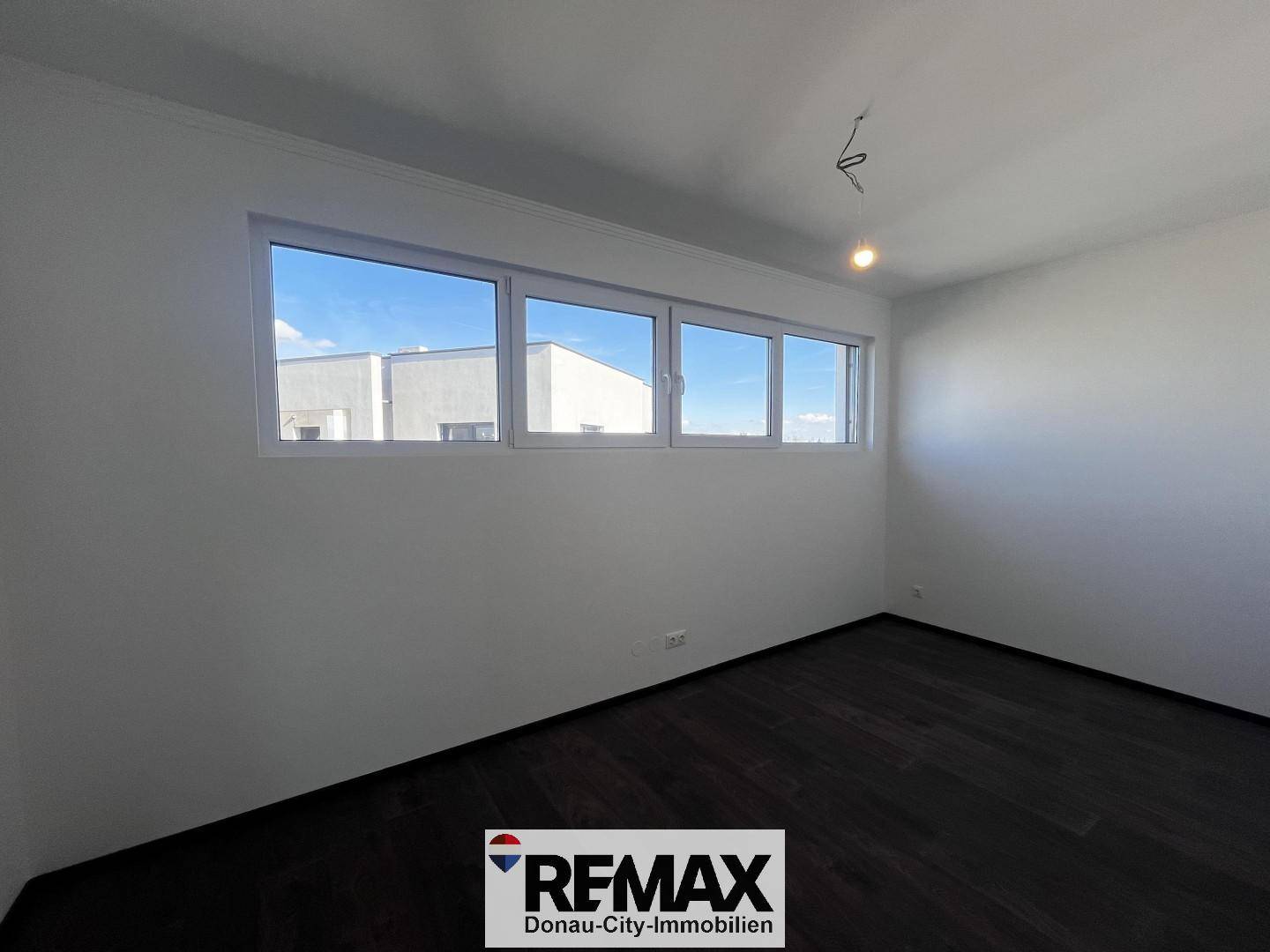 Geräumiges Zimmer mit breitem Fensterband und dunklem Holzboden, ideal als Schlafzimmer.