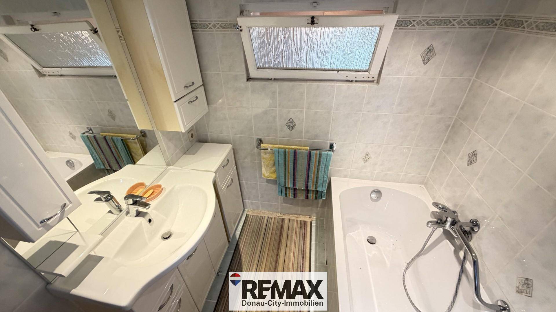 Badezimmer mit Badewanne, Waschbecken und Dachfenster, gefliest in hellen Tönen.