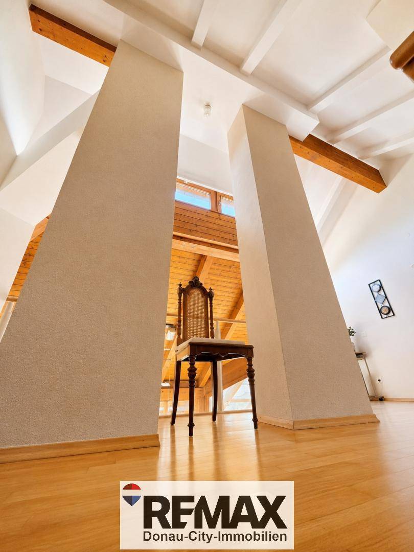 Offener Flurbereich im Obergeschoss mit Holzboden, hohen Decken und einem dekorativen Stuhl.