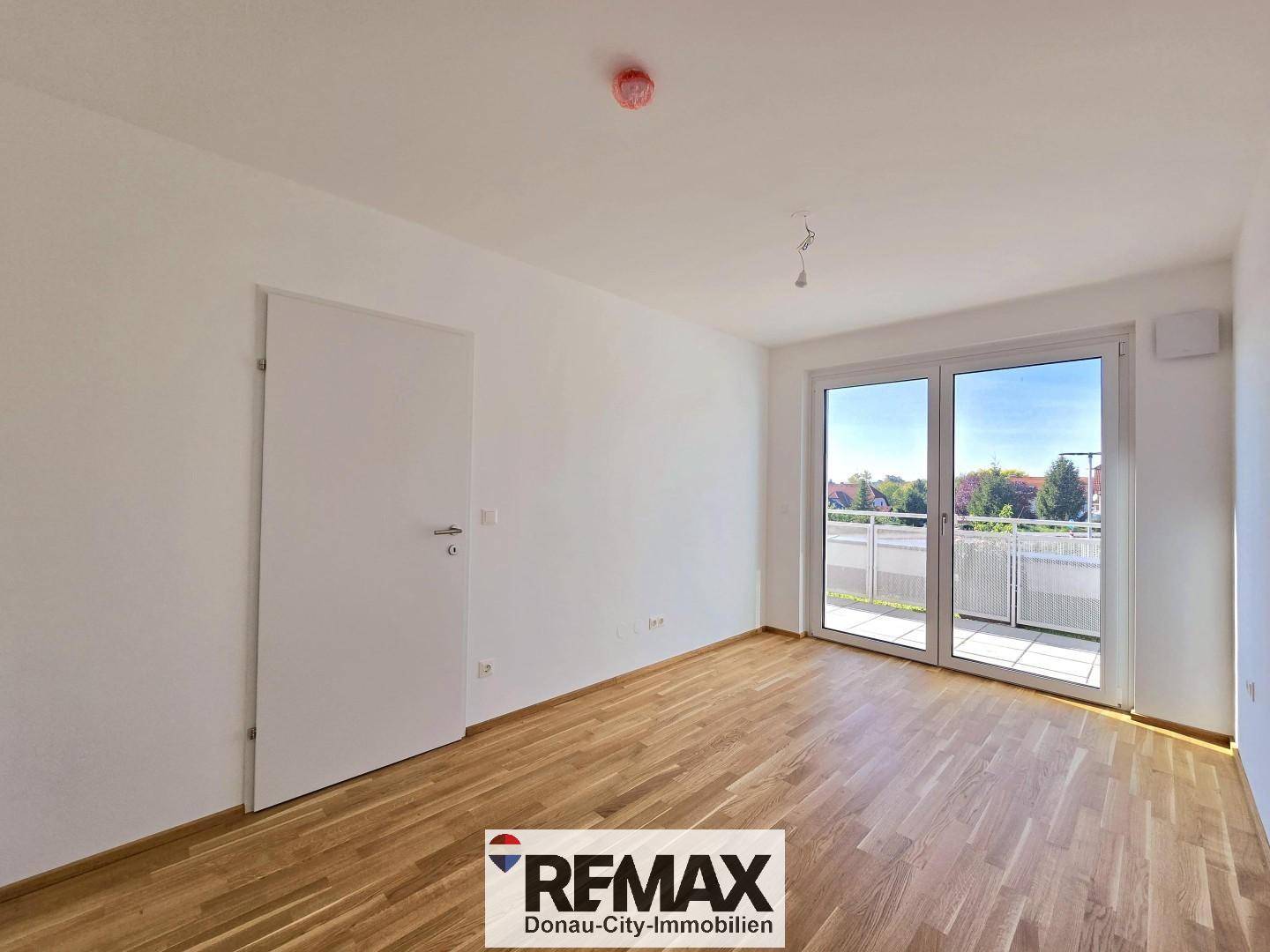 Leeres Schlafzimmer mit hellem Holzboden und großen Fenstern zum Balkon.