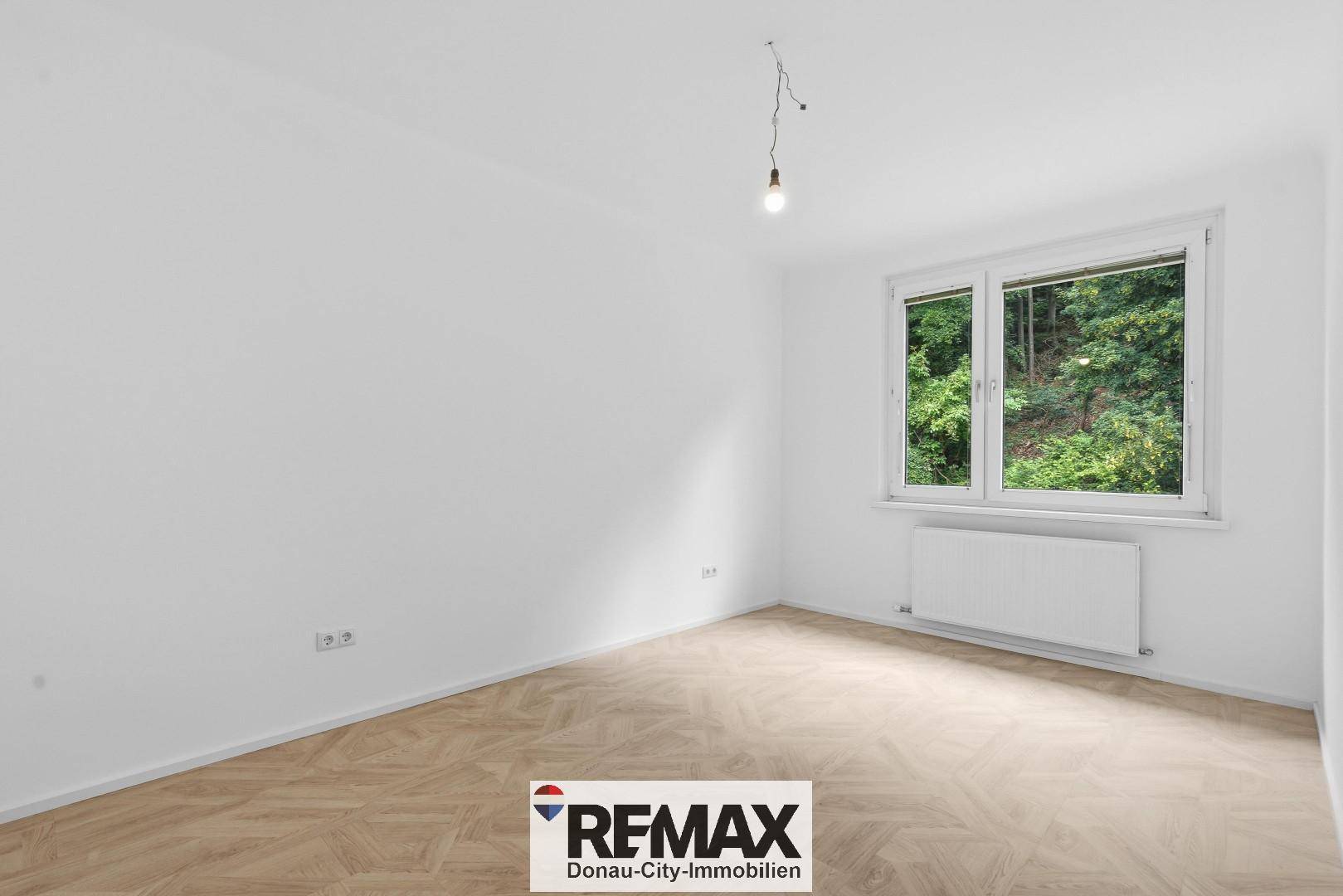 Helles Schlafzimmer mit großem Fenster, Blick ins Grüne und modernem Fischgrätparkett.