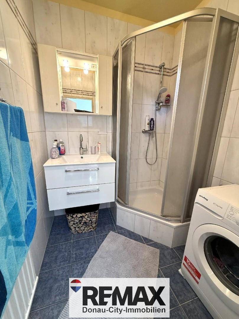 Badezimmer mit Duschkabine, Waschbecken und Waschmaschine, gefliest in Blau und Weiß.