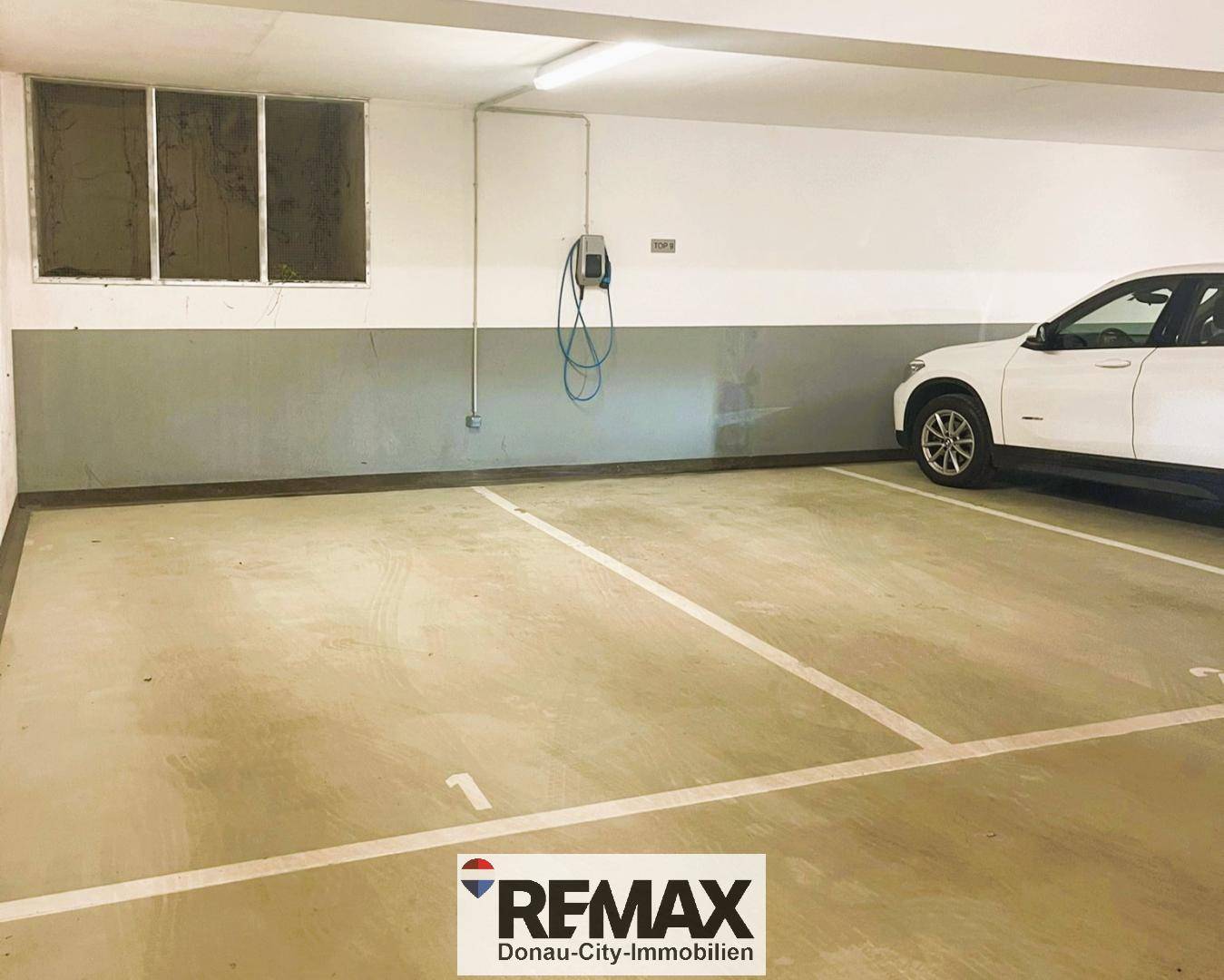 Geräumiger Tiefgaragenstellplatz mit Ladestation für Elektrofahrzeuge und einem geparkten Auto.