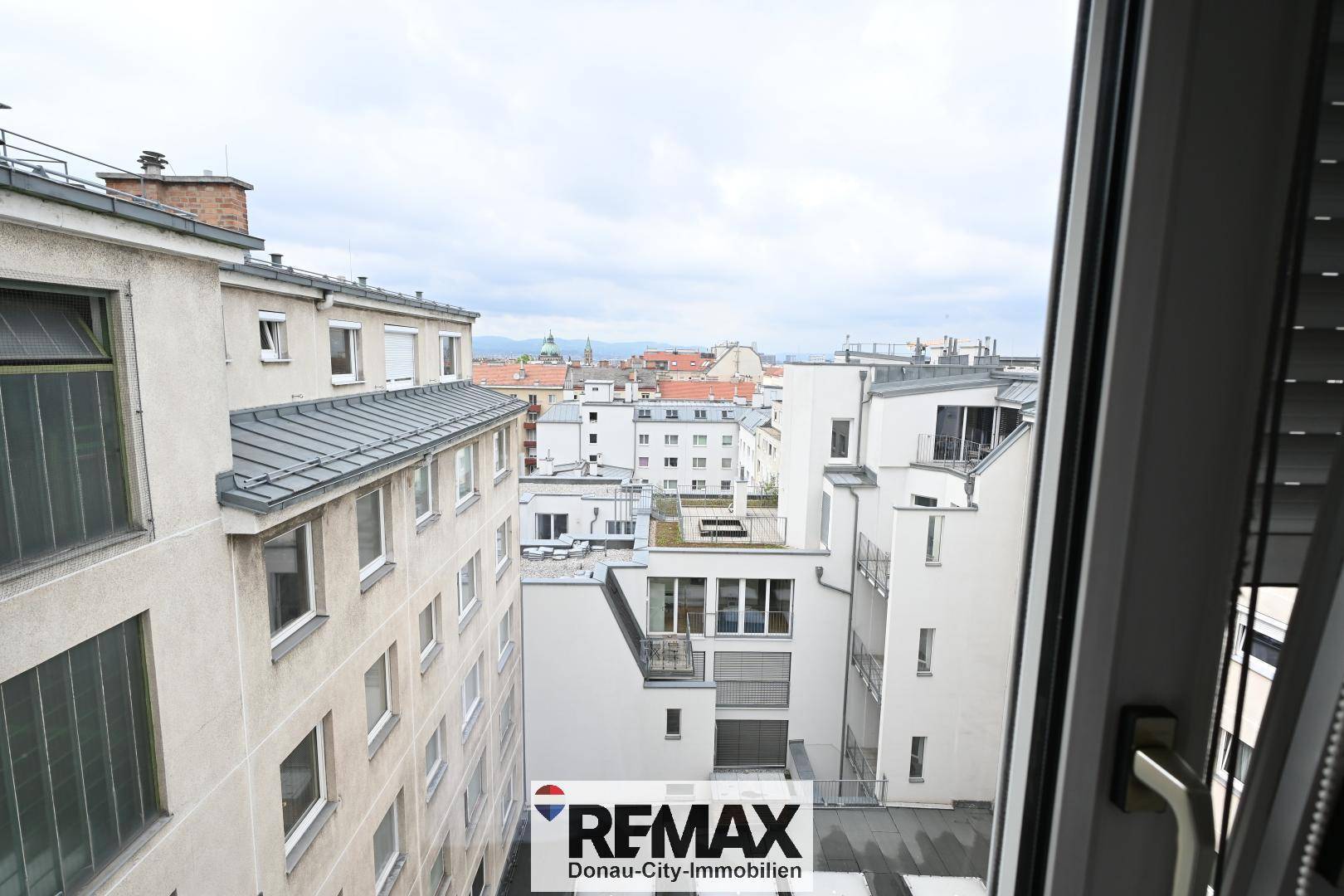Blick aus dem Fenster auf eine dichte städtische Bebauung mit vielen Dächern und Gebäuden.