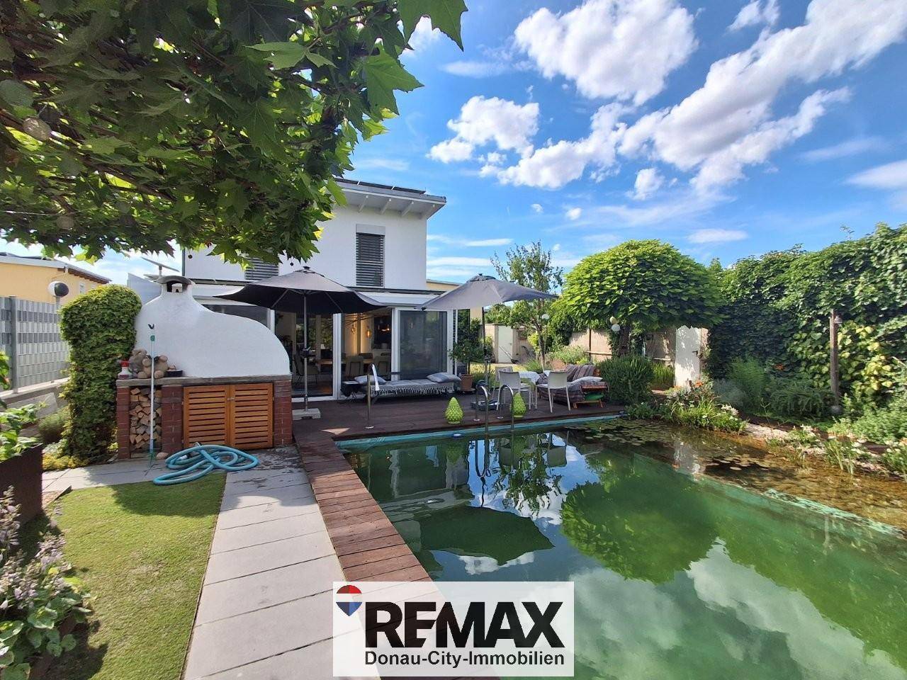 Geräumige Terrasse mit Außenküche, Pizzaofen und großem Schwimmteich im Garten.