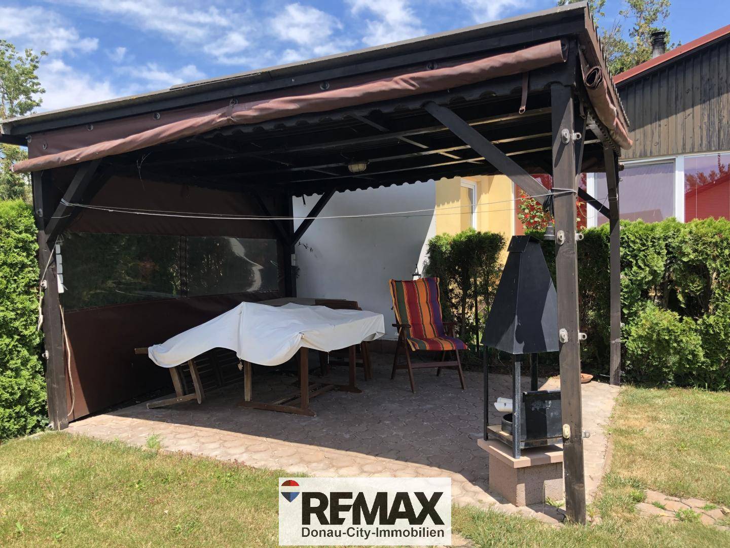Gemütlicher überdachter Terrassenbereich mit Tisch und bunten Gartenstühlen.