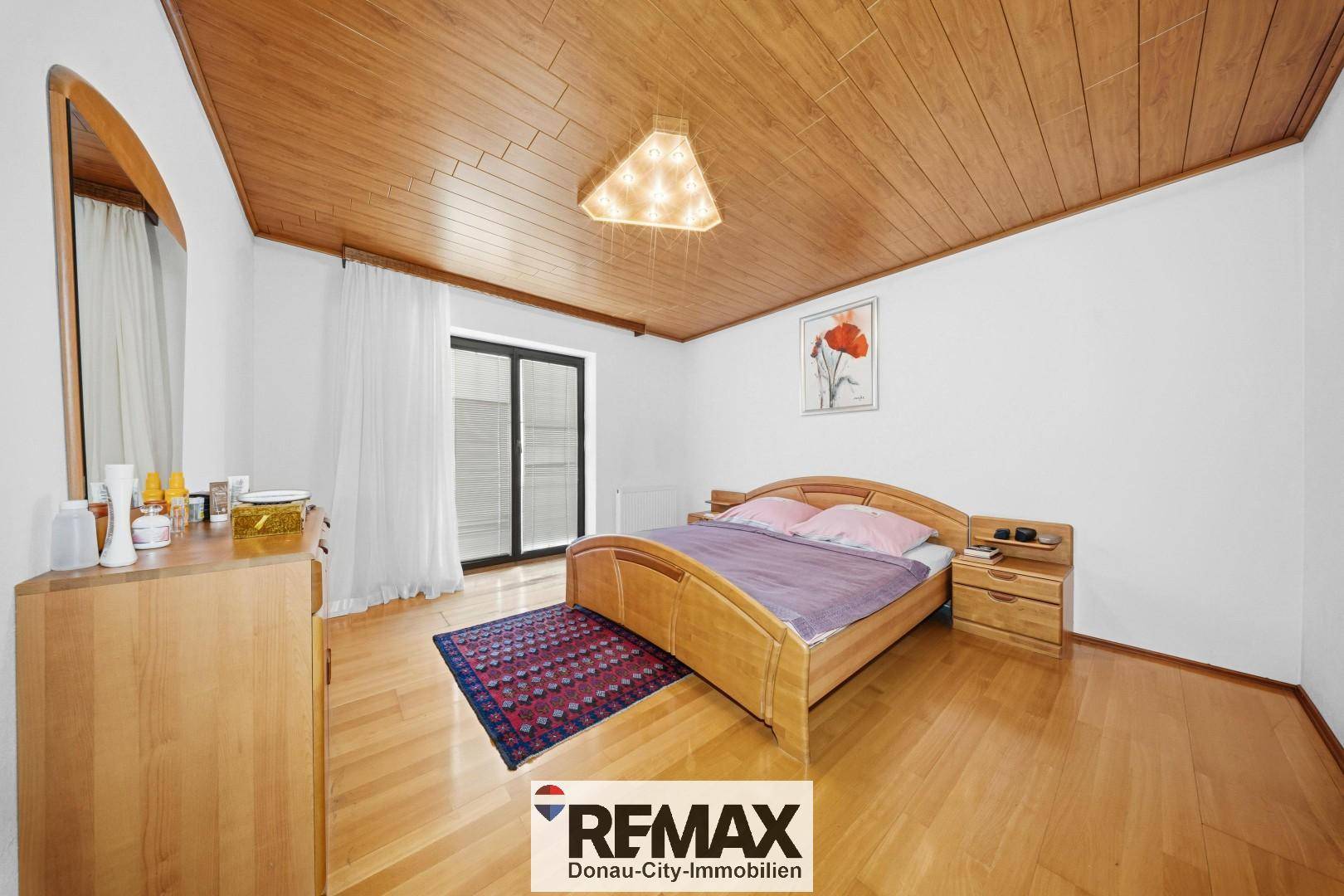 Schlafzimmer mit Holzdecke, Parkettboden und Zugang zum Balkon, gemütlich eingerichtet.
