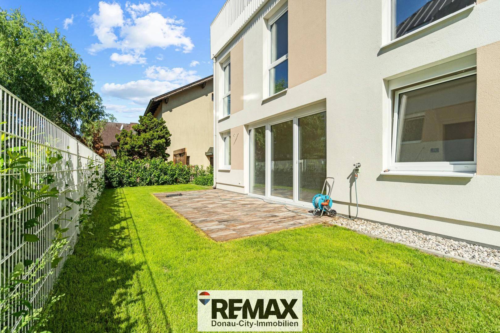 Kleiner Gartenbereich mit Rasenfläche und gepflasterter Terrasse hinter dem modernen Wohnhaus.