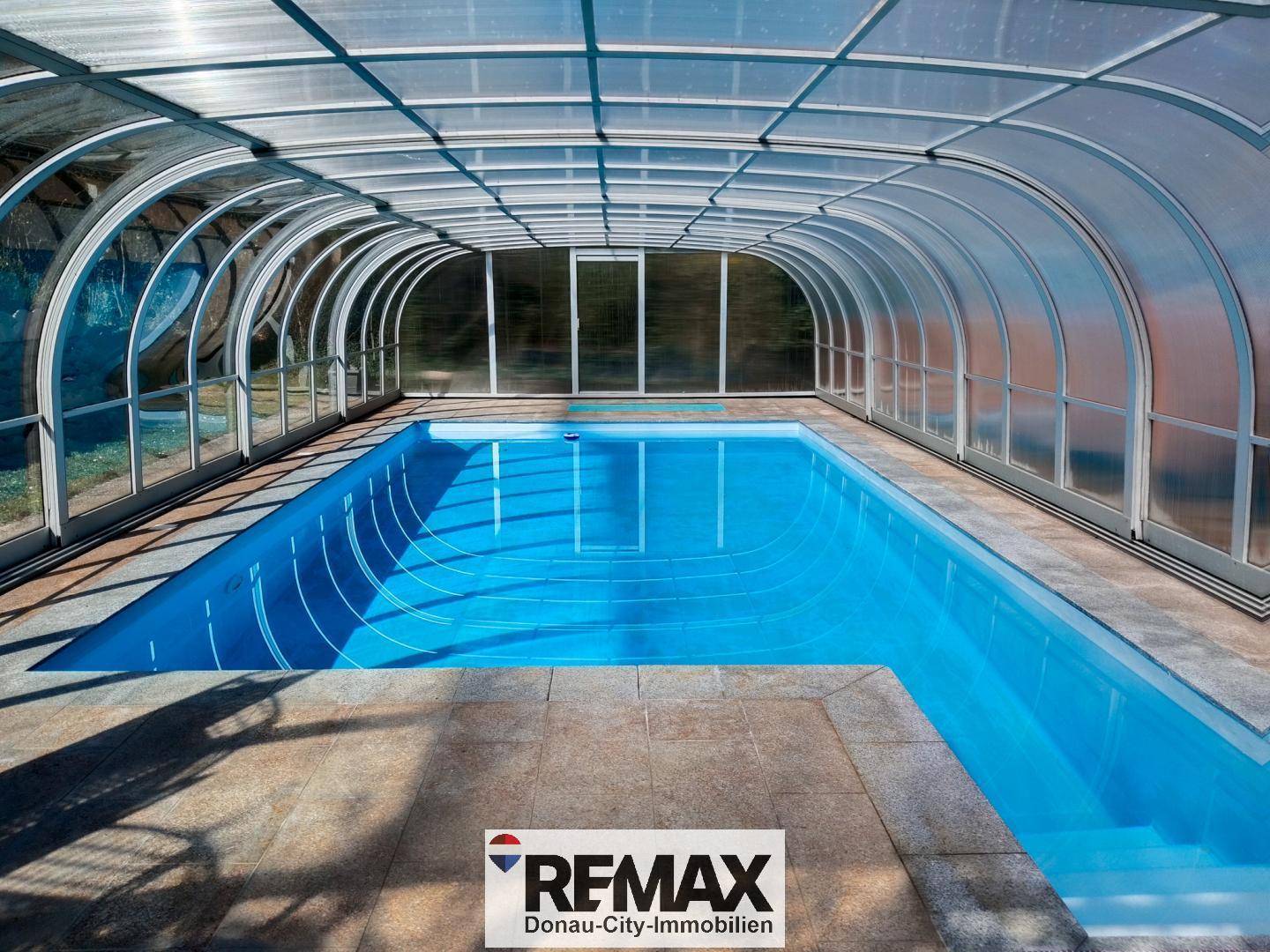 Überdachtes Schwimmbad mit klarem Wasser und großzügiger Glasüberdachung für ganzjährigen Badespaß.