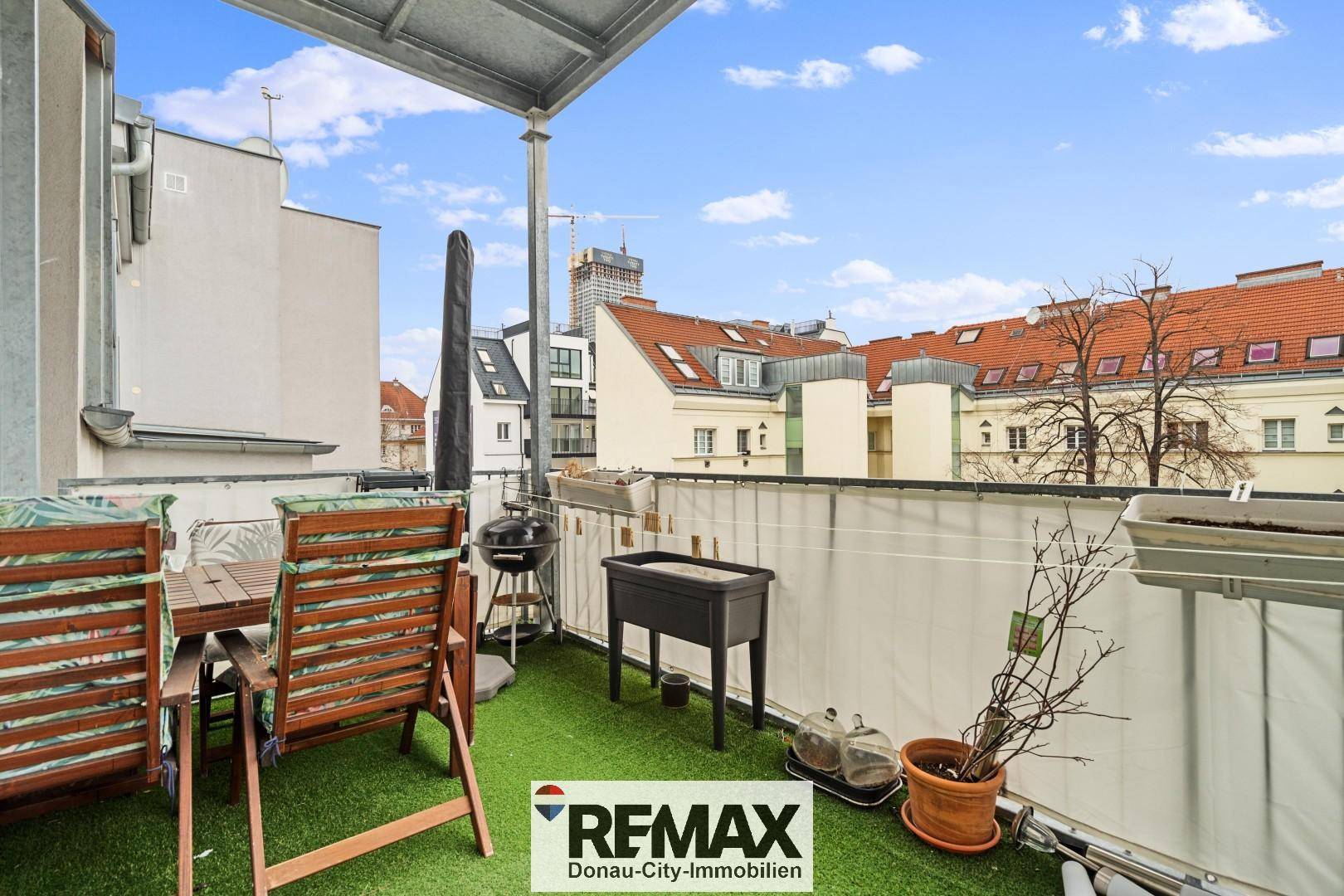 Überdachter Balkon mit Kunstrasen, Grill und Gartenmöbeln, bietet einen Stadtblick.