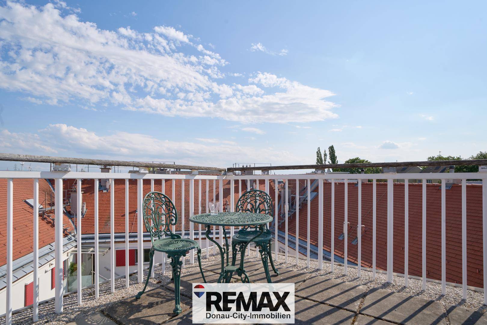 Sonnige Dachterrasse mit schmiedeeisernen Möbeln und weitem Blick über die Dächer.