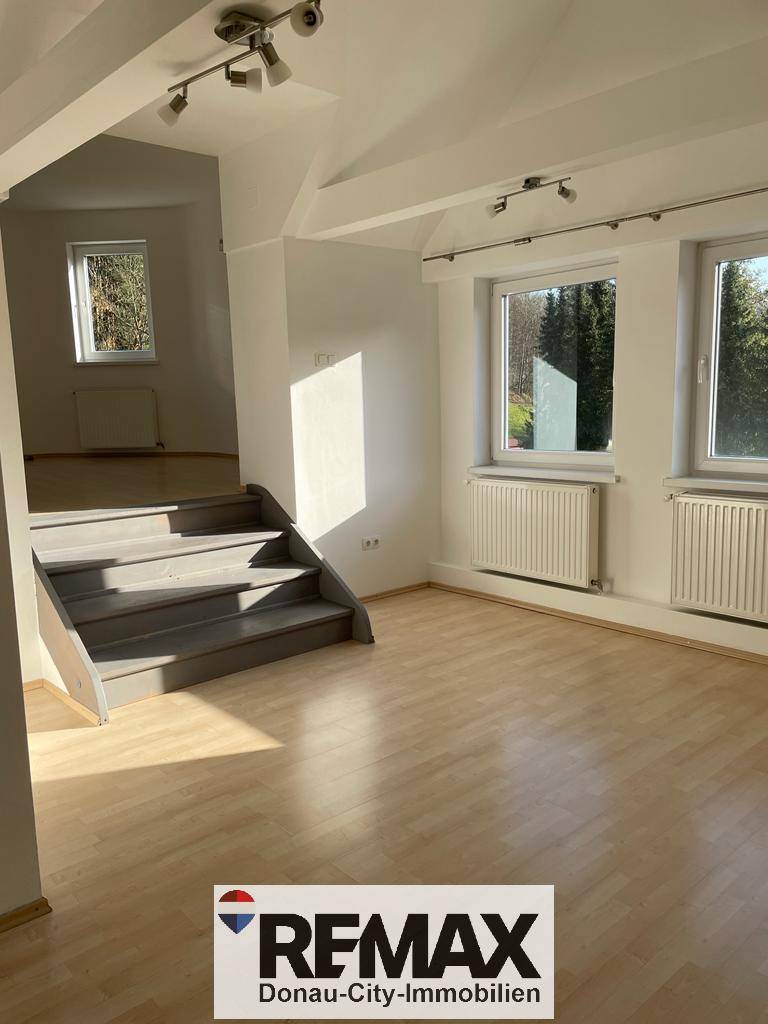 Heller Wohnbereich mit Holzfußboden, Treppe und großen Fenstern mit Blick ins Grüne.
