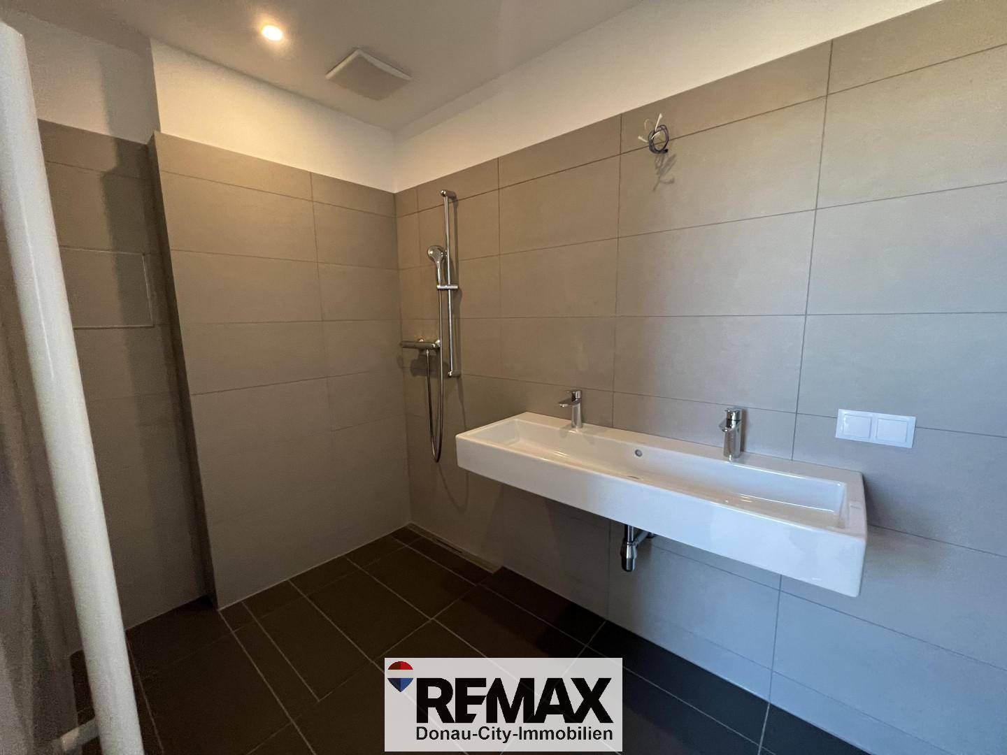 Modernes Badezimmer mit begehbarer Dusche, schwebendem Waschbecken und grauen Fliesen.