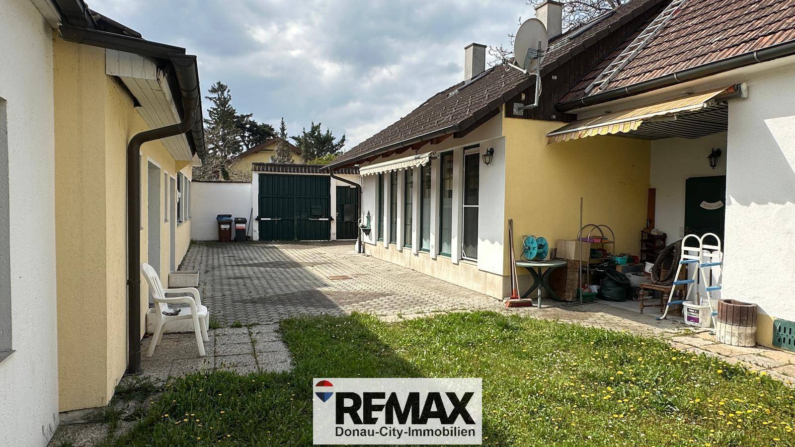 Hinterhofbereich mit kleiner Rasenfläche, gepflastertem Weg und Markise am Haus.