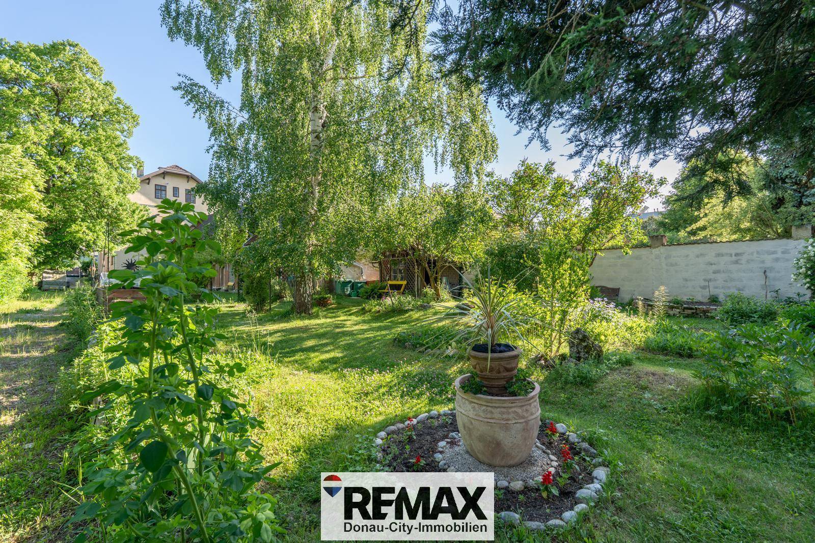 Gepflegter Gartenbereich mit verschiedenen Pflanzen, Bäumen und einem dekorativen Pflanzgefäß.