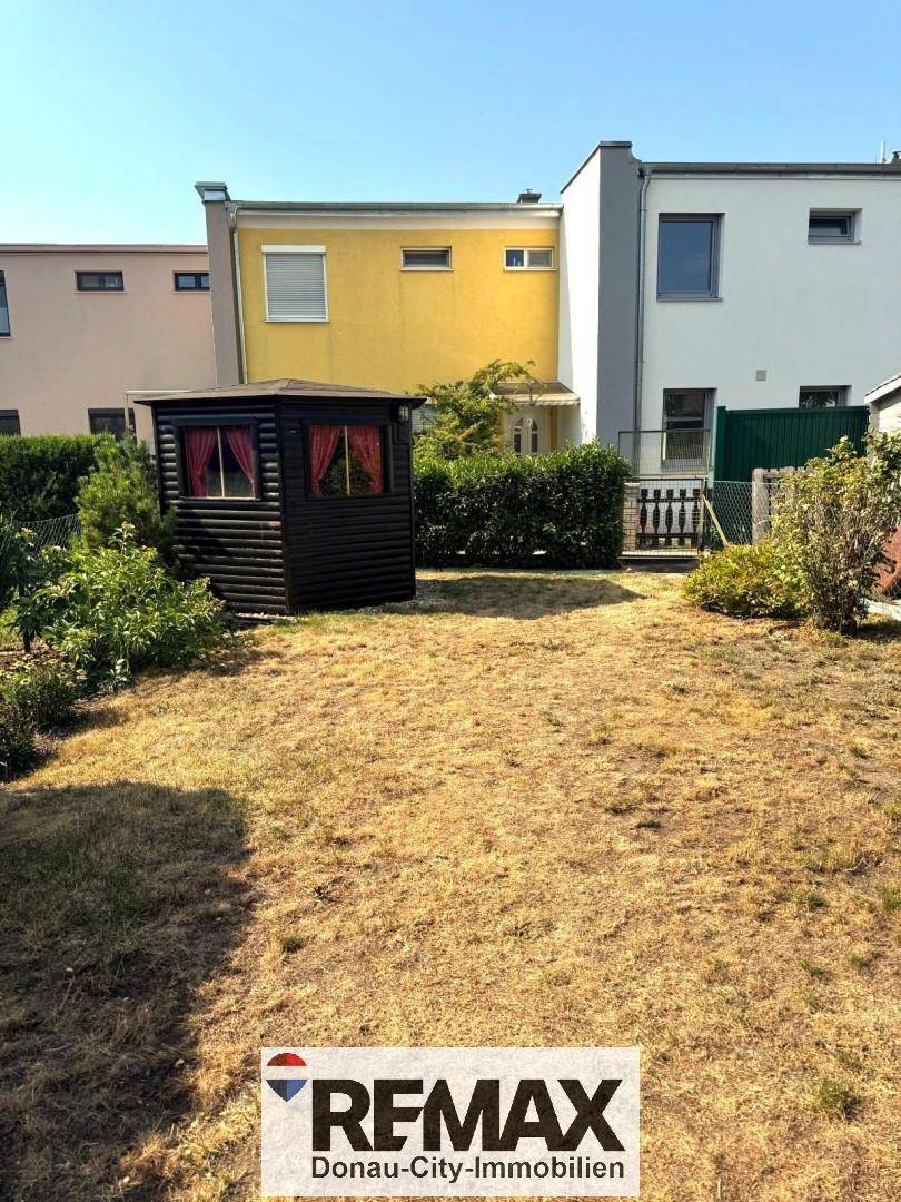 Hinterhofgarten mit kleinem Gartenhaus und Zaun, umgeben von trockener Rasenfläche.