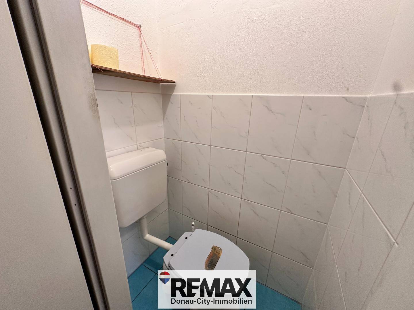 Kleines WC mit weißen Wandfliesen und einem blauen Boden, einfach ausgestattet.