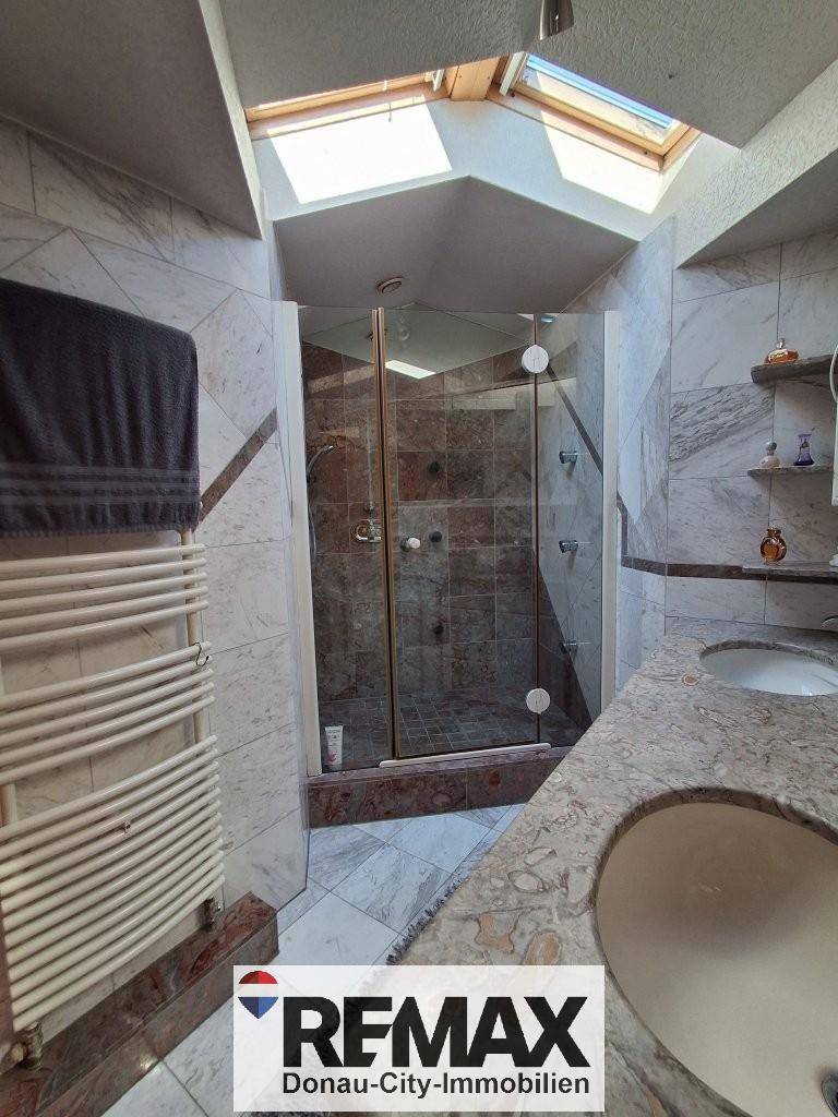 Modernes Badezimmer mit Duschkabine, Einzelwaschbecken und Dachfenster, das für viel Helligkeit sorgt.
