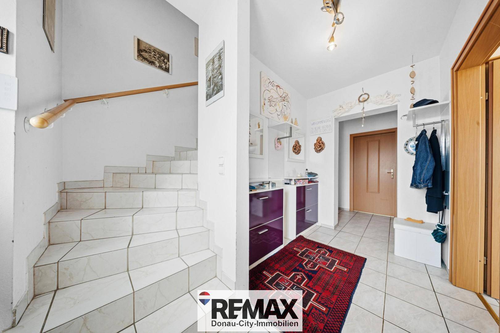 Eingangsbereich mit gefliestem Boden, Treppe zum Obergeschoss und Garderobe.