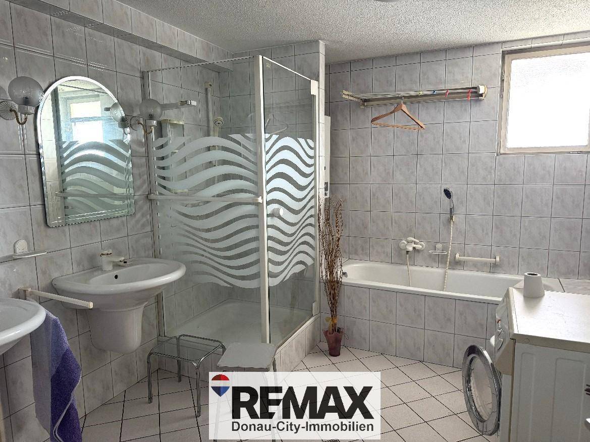Gefliestes Badezimmer mit Badewanne, Duschkabine, Waschbecken und Fenster.