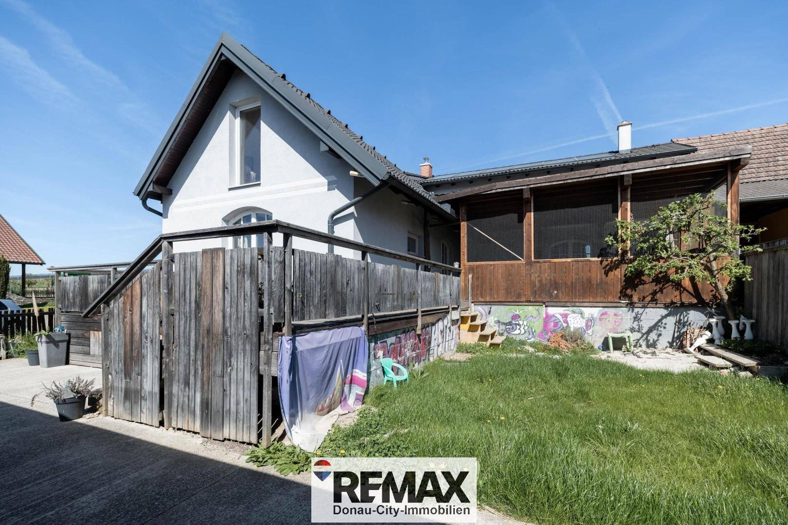 Rückseite des Hauses mit überdachter Holzloggia, Treppe und kleinem Gartenbereich.