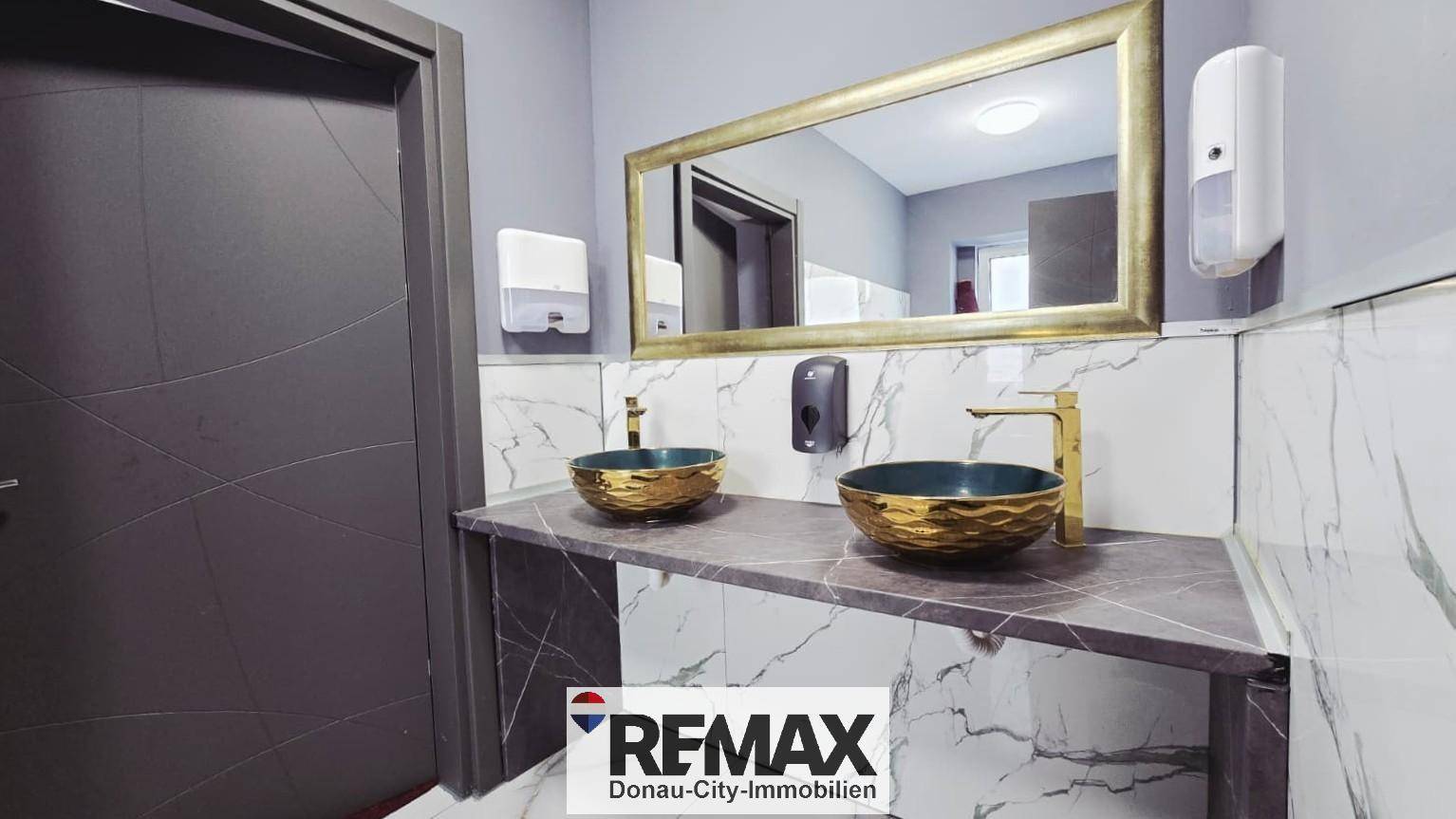 Modernes Badezimmer mit zwei goldenen Waschbecken, einem großen Spiegel und eleganten Marmorfliesen.