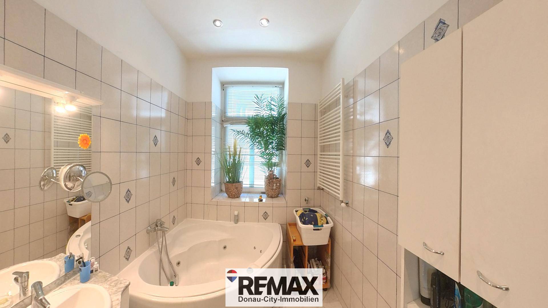 Gefliestes Badezimmer mit Whirlpool-Badewanne, Einzelwaschbecken und Fenster für Tageslicht.