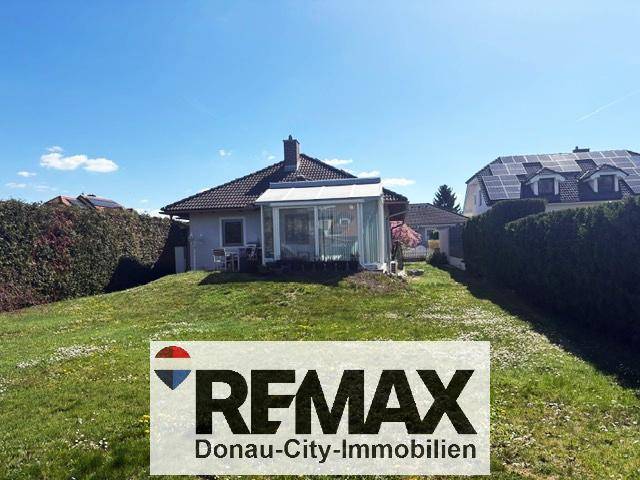 Rückansicht des Hauses mit Wintergarten und weitläufigem Gartenbereich unter strahlendem Himmel.