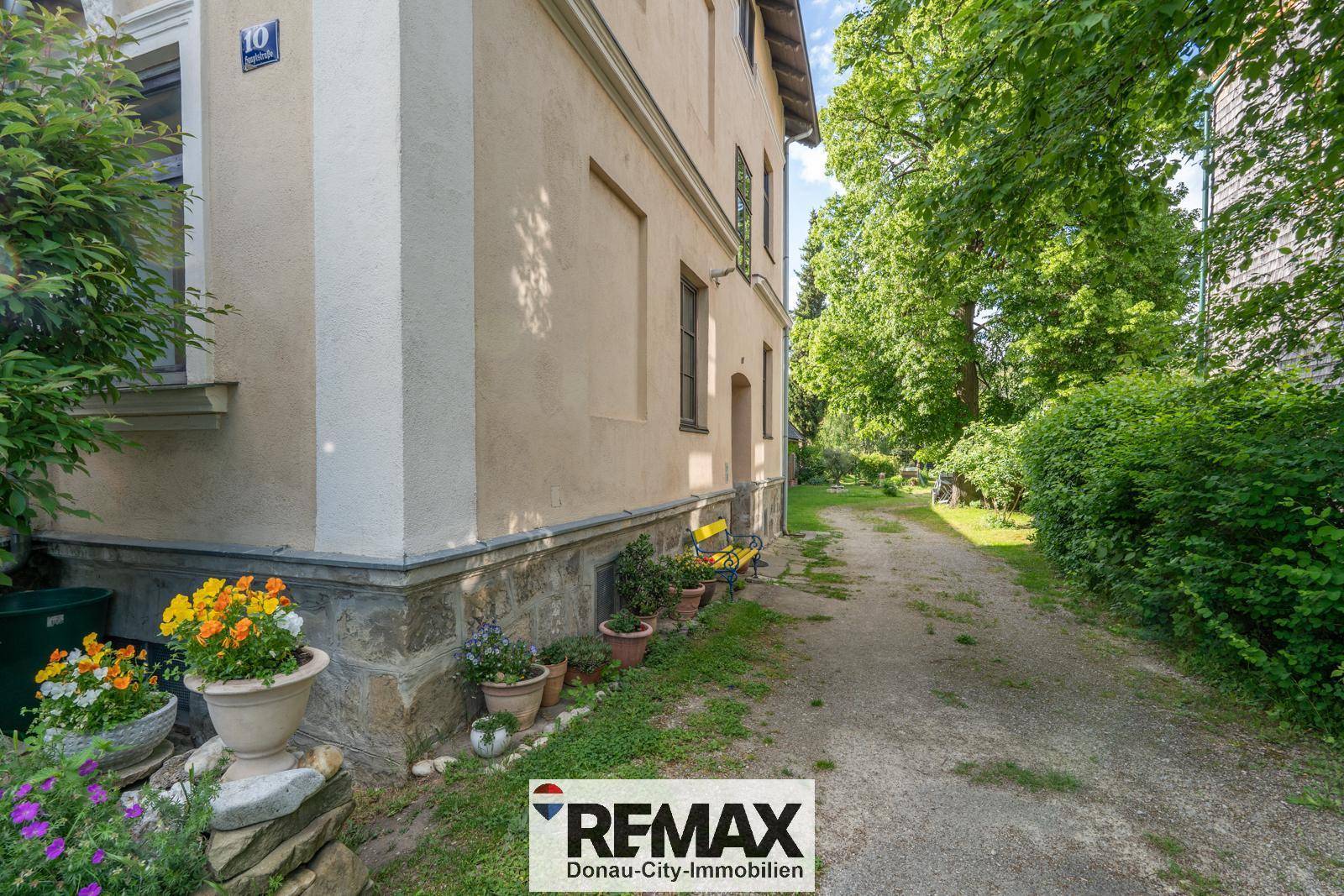 Seitenansicht des Hauses mit Kiesweg, Topfpflanzen und einer gepflegten Hecke.