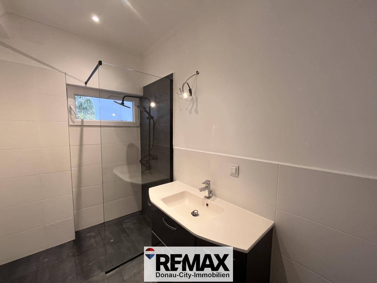 Modernes Badezimmer mit begehbarer Dusche, Einzelwaschbecken und Fenster für Tageslicht.
