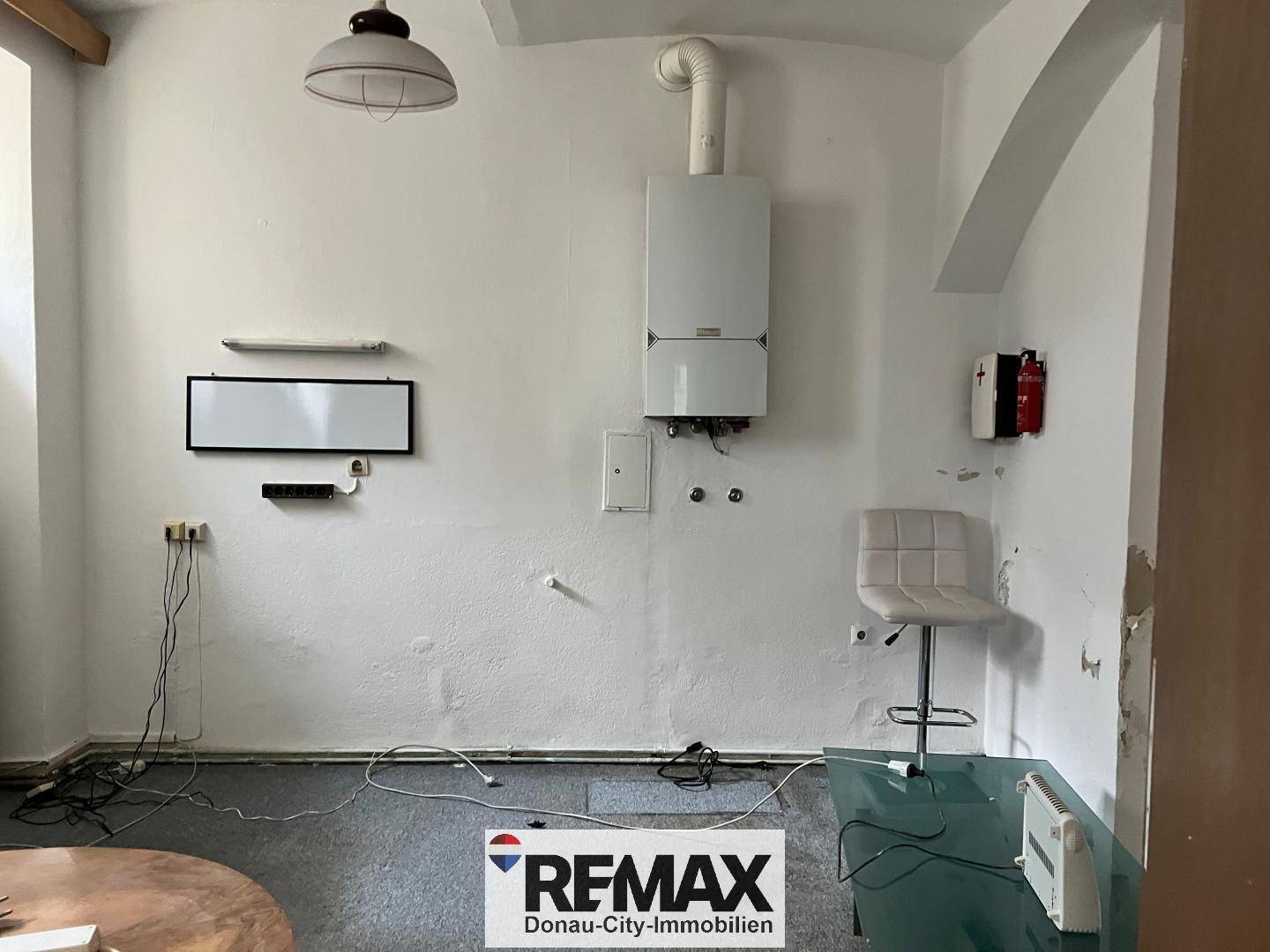 Einfacher Raum mit Heizungsanlage, Teppichboden und einem kleinen Tisch, ideal als Abstellraum.