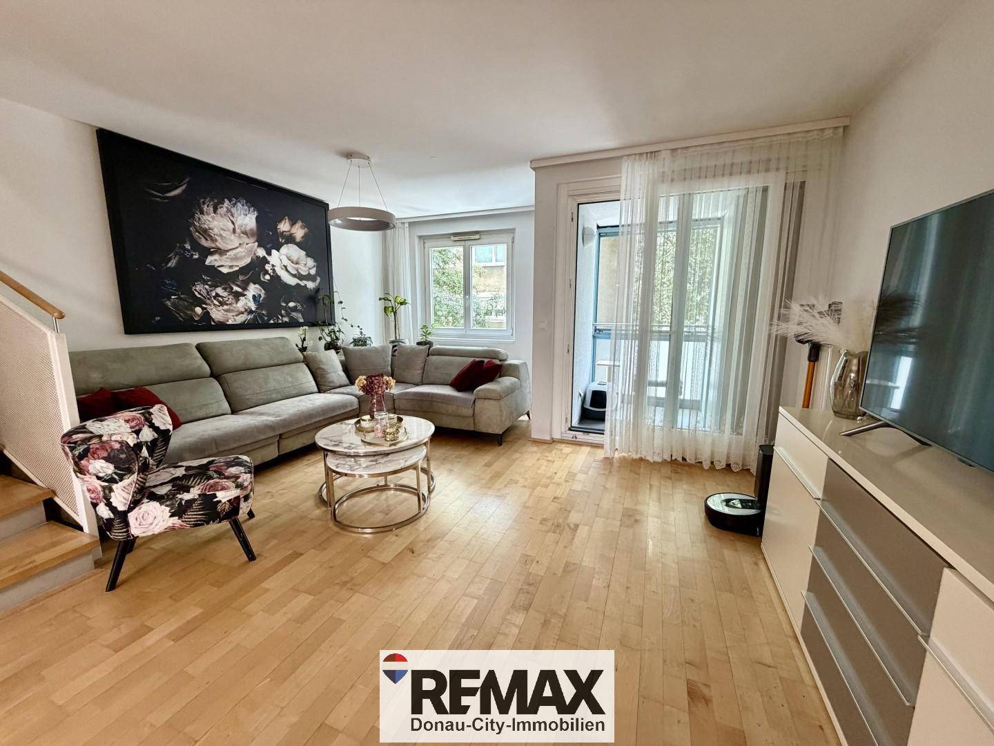 Helles Wohnzimmer mit Parkettboden, bequemer Couch und Zugang zu einem Balkon.