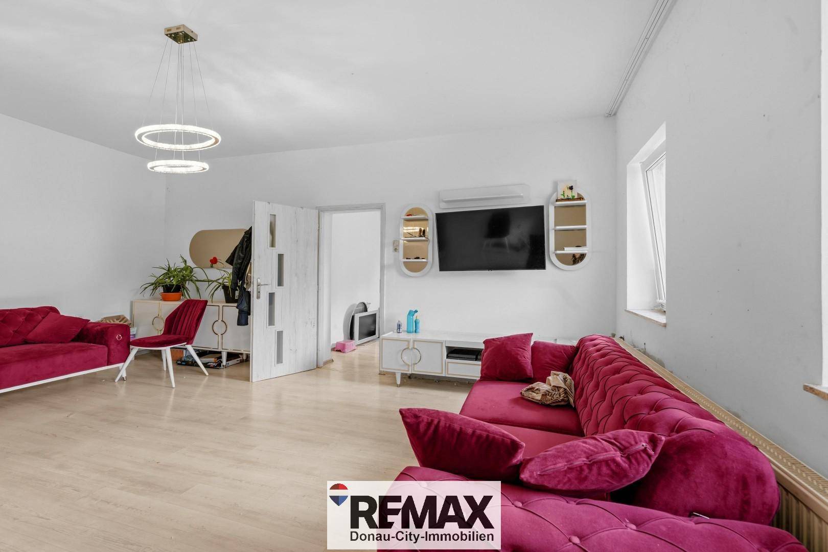 Helles Wohnzimmer mit modernem Laminatboden, roten Sofas und Wandmontage für TV.