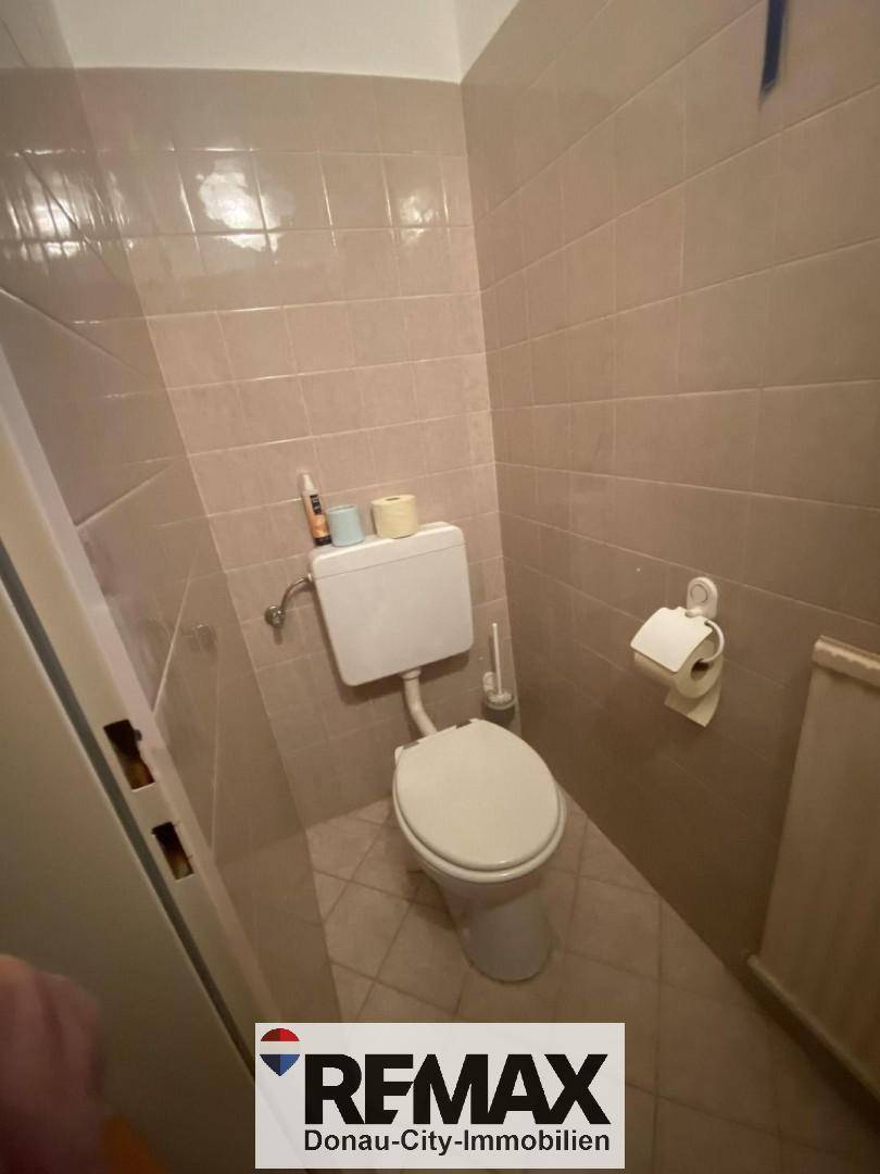 Separate Toilette mit WC und Heizkörper, ausgestattet mit beigefarbenen Fliesen.