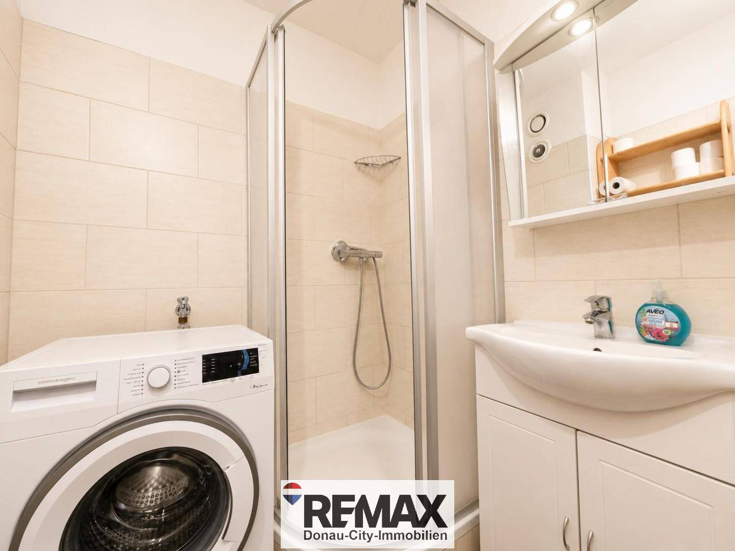 Helles Badezimmer mit Duschkabine, Waschbecken und Waschmaschine.