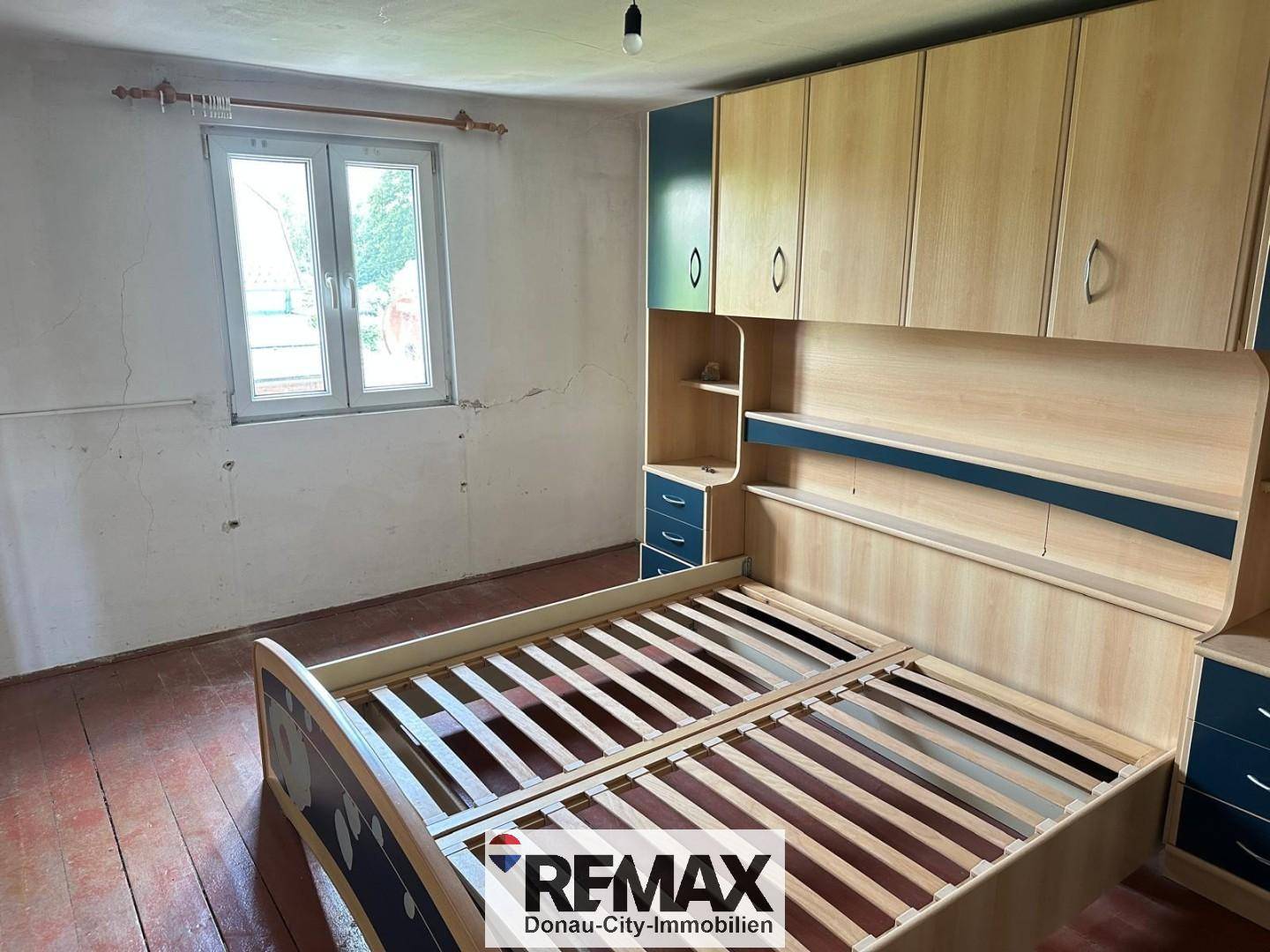 Schlafzimmer mit eingebauten Holzschränken und einem Bettrahmen, Wände sind renovierungsbedürftig.