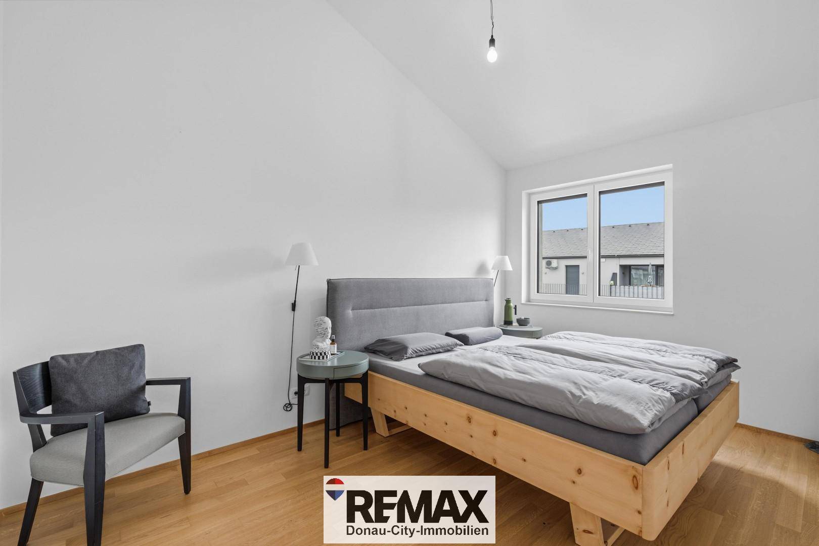 Modernes Schlafzimmer mit Holzboden, schrägen Wänden und einem Fenster mit Blick nach draußen.
