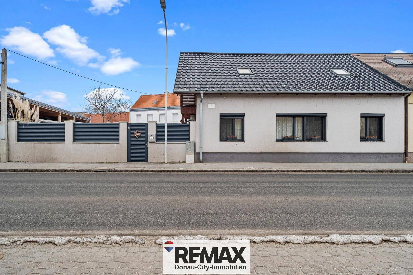 Ansicht des Einfamilienhauses von der Straße mit grauer Fassade und Dachziegeln.