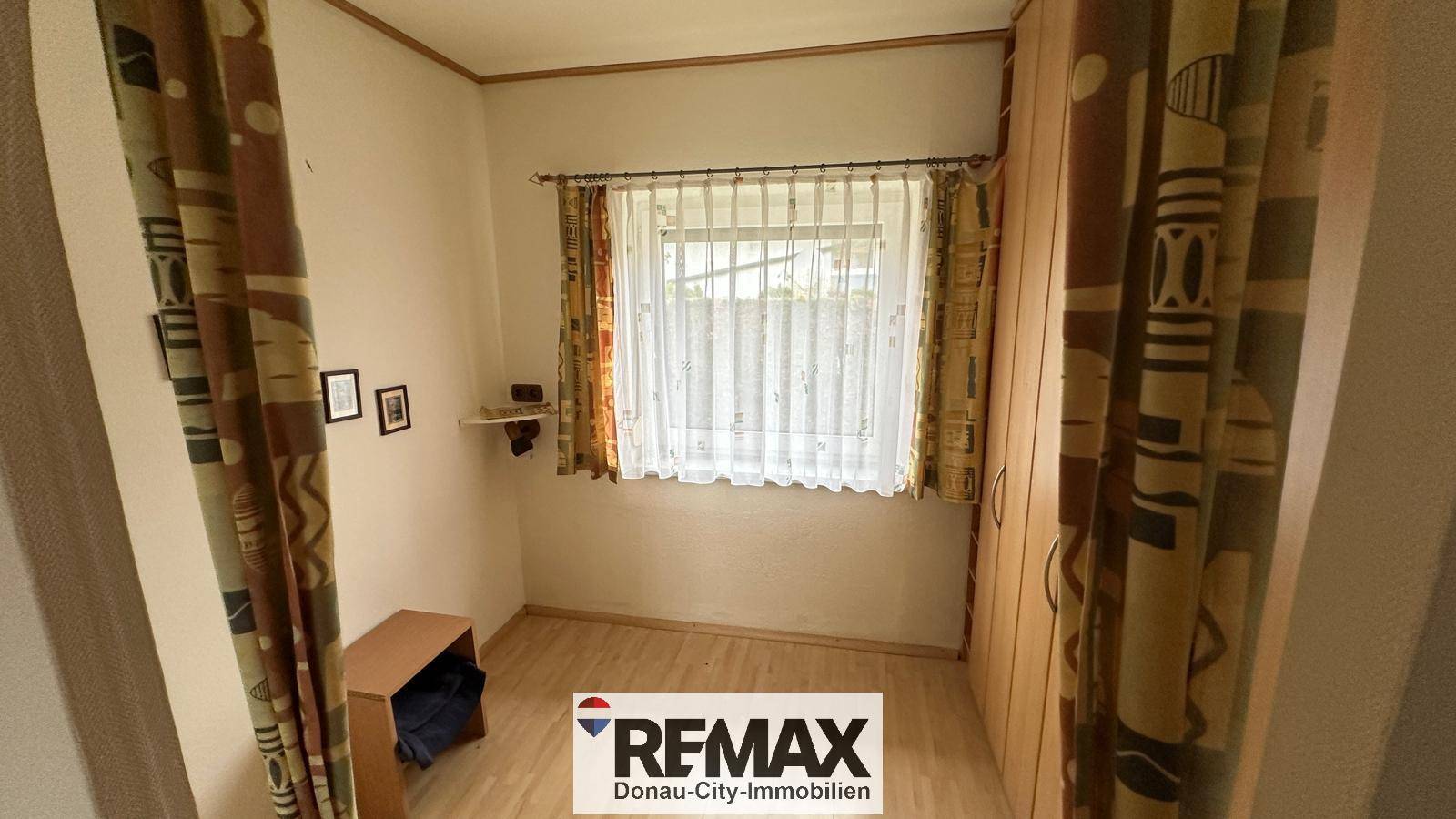 Helles Schlafzimmer mit Laminatboden, Fenster und einem Kleiderschrank.