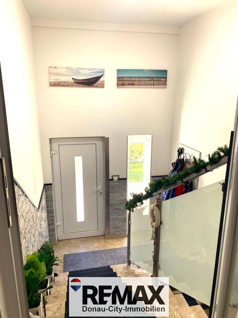 Eingangsbereich mit Treppe und moderner Glastür, hell und einladend gestaltet.