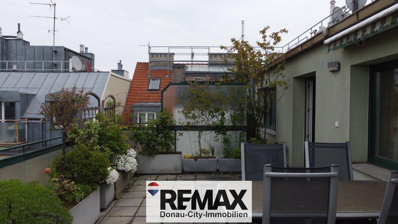 Terrasse mit Sitzgelegenheiten und Blick auf die umliegenden Dächer und Gebäude.