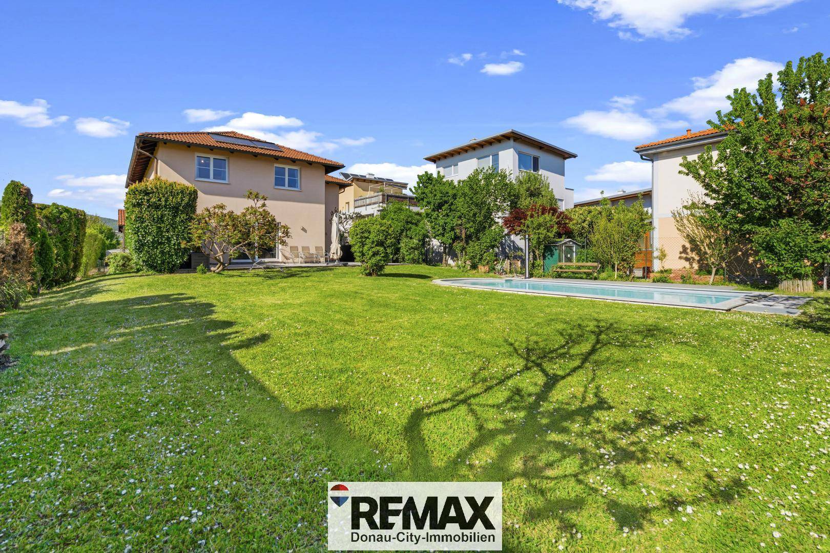 Gepflegter Garten mit Rasenfläche, Pool und dem Wohnhaus im Hintergrund.