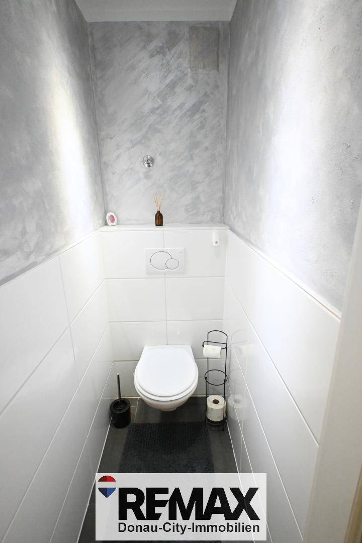Separates WC mit wandhängender Toilette und einer modern gestalteten Akzentwand in Grau.