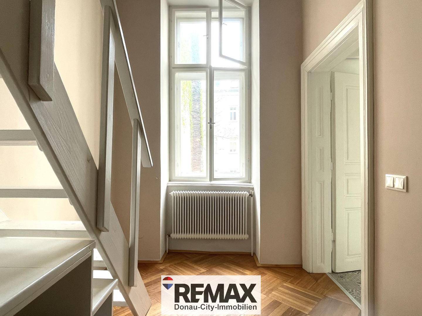 Heller Flur mit Holztreppe, Fenster und Parkettboden.