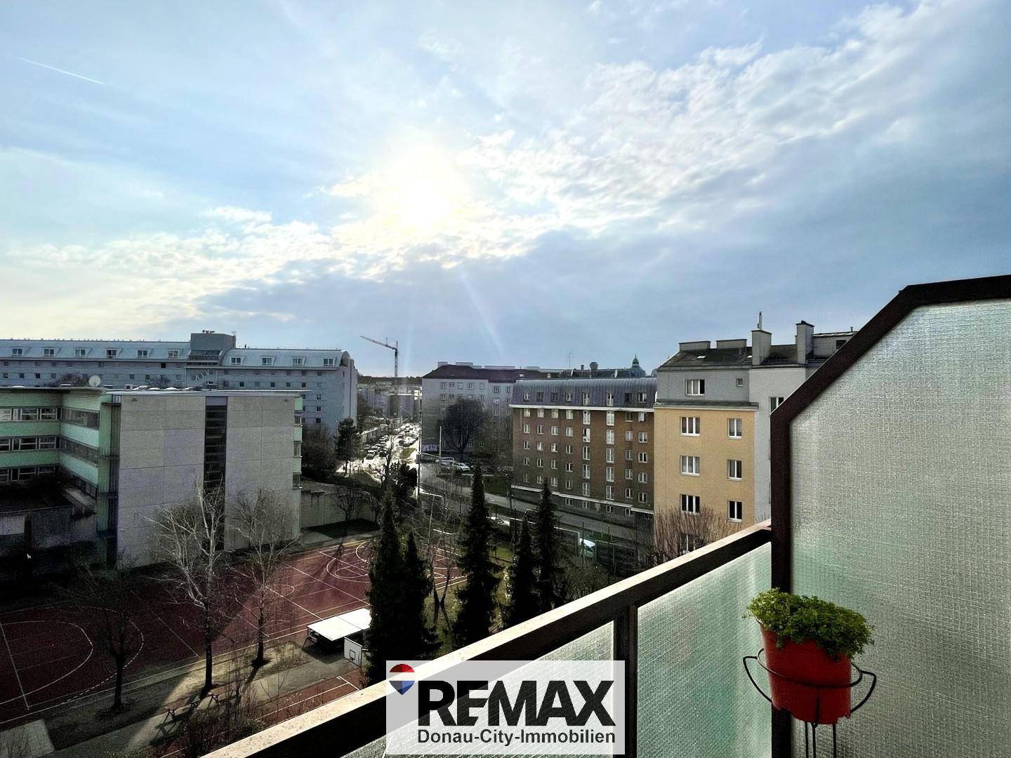 Ausblick von einem Balkon auf eine städtische Umgebung mit Gebäuden, Bäumen und einem Sportplatz.